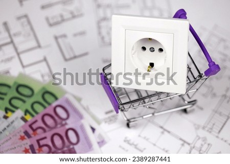 European standard EU outlet in small shopping cart on blueprints of residential house plan close up. Concept of shopping and electricity devices Royalty-Free Stock Photo #2389287441