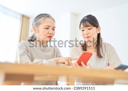 A senior woman and a young woman looking anxiously at their smartphone screens Royalty-Free Stock Photo #2389291511