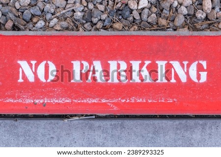 Close up of a red "No Parking" sign with white lettering painted onto a sidewalk curb.