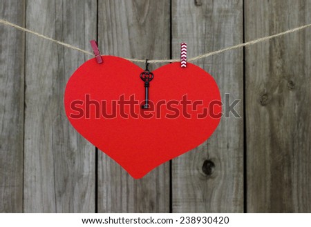Large red heart and black iron key hanging on clothesline by shabby wooden background