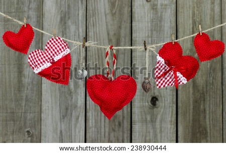 Red and white country fabric hearts and silver and bronze heart locks hanging on clothesline by shabby wooden background