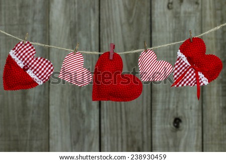 Red and white candy cane striped and checkered country fabric hearts hanging on clothesline by shabby wooden background