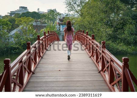 Red bridge The Huc in Hoan Kiem lake, Hanoi, with a girl in long dress walking on the bridge Royalty-Free Stock Photo #2389311619