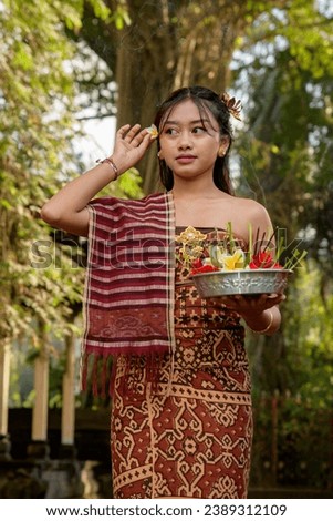 A woman in a red and gold sarong and a flower in her hair offering prayers in a Balinese temple
