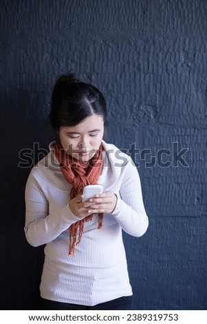 Portrait of a happy Chinese woman leaning against a using her phone. Lifestyle image.