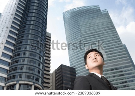 Chinese business man in modern Asian city. Asian businessman smiling  looking at the camera with skyscraper office buildings above. Royalty-Free Stock Photo #2389336889