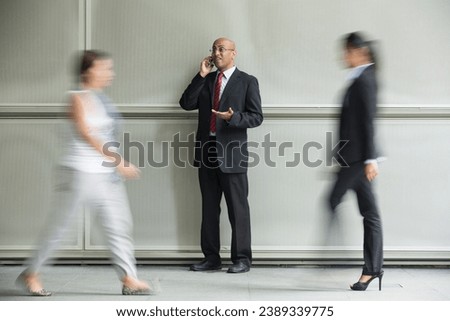 Indian Business man using a Cell Phone with Motion Blurred People walking past.