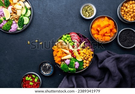 Vegan buddha bowl with sweet potato, quinoa, chickpeas, soybeans edamame, tofu, corn, cabbage, radish, broccoli and seeds, black table background, top view. Autumn or winter healthy vegetarian food