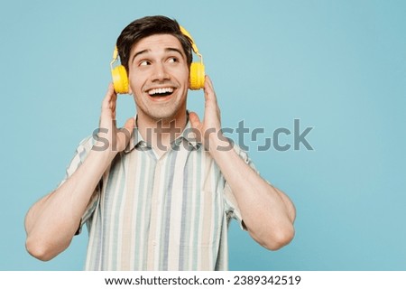 Young happy amazed fun man he wears striped shirt casual clothes listen to music in headphones look aside on area isolated on plain pastel light blue cyan background studio portrait. Lifestyle concept