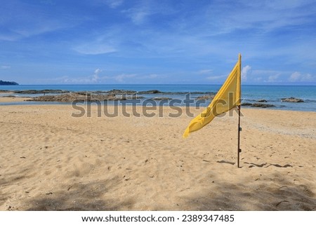 The yellow life saving flags on flagpole flutters in the wind against blue sky, Flag and shadow of tree on sand. Yellow flag is planted on the beach as a warning sign about safety  playing in the sea.