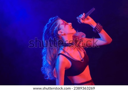 Attractive girl rock singer sings with a microphone. Glam rock style. Place for text. Royalty-Free Stock Photo #2389363269