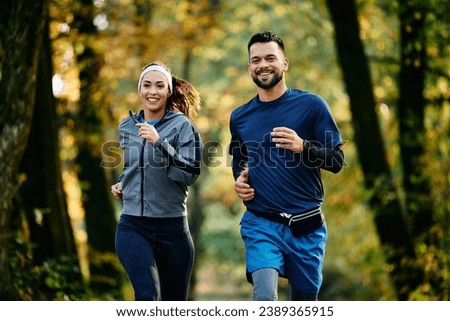 Happy athletic couple jogging during autumn day in the park. Royalty-Free Stock Photo #2389365915