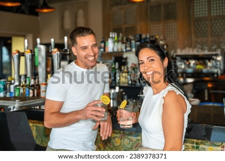 Horizontal portrait of a caucasian couple smiling at camera drinking cocktails in a luxury bar