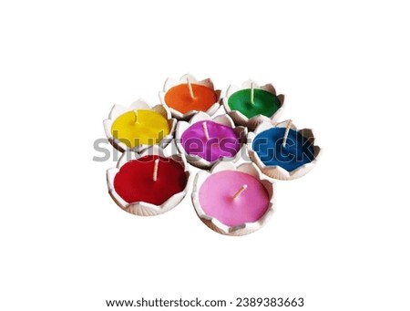 In the picture are colored candles in a white lotus pot. There are orange, green, pink, yellow, purple, blue, red. In the center of the candle there is a white string for lighting.