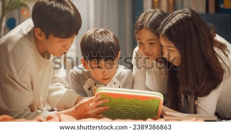 Young Beautiful South Korean Family Spending Free Time Together at Home, Watching Cartoons Online and Playing Educational Video Games Together with Their Talented Children on Tablet Computer