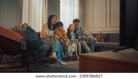 Happy Korean Family At Home: Mother And Father Watching Funny Family Television Show And Laughing With Their Little Son And Daughter On The Couch. Siblings Having Fun With Parents In Living Room. Royalty-Free Stock Photo #2389386867