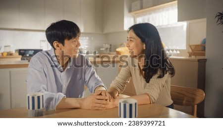 Attractive Korean Young Couple Sitting at Home, Talking. Boyfriend and Girlfriend Having Fun Conversations in the Kitchen. Family with Healthy Lifestyle Looking at Camera and Smiling