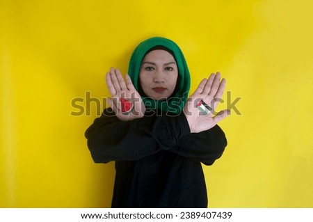 Muslim woman shows crossed arms painted with Palestinian flag and watermelon slices over yellow background. Stop war and humanity concept