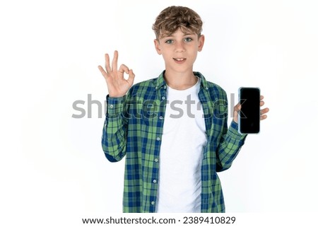 caucasian kid boy wearing plaid shirt holding in hands cell showing ok-sign