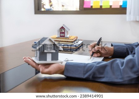 Real estate agents hand use pen, holding home model, explains the business contract for signing a business contract, renting, buying, mortgage, loan or home insurance.