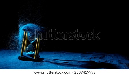 Hourglass is sand of time age, Life pour blue sand into hourglass to add more limited time. Deadline extended time management hope concept hour glass. Black background shadow life clock passing by Royalty-Free Stock Photo #2389419999