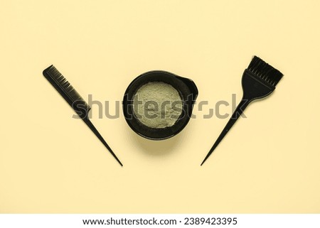 Bowl with henna, comb and brush on yellow background