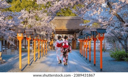Young Japanese women in traditional Yukata dress stroll by Hirano-jinja Shrine in Kyoto, Japan during full bloom cherry blossom season Royalty-Free Stock Photo #2389431867