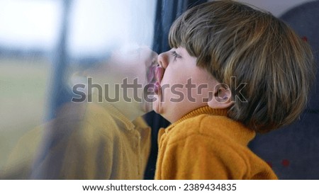 Bored funny small boy with face glued on trian window. Mouth and lips pressed on glass and staring at landscape scenery pass by in transportation