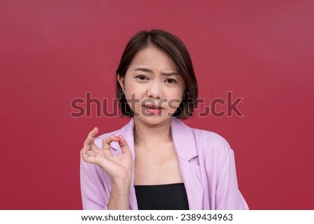 A snobbish young woman making a condescending explanation to someone she looks down on. A mean lady looking repulsed. Studio shot with burgundy background. Royalty-Free Stock Photo #2389434963