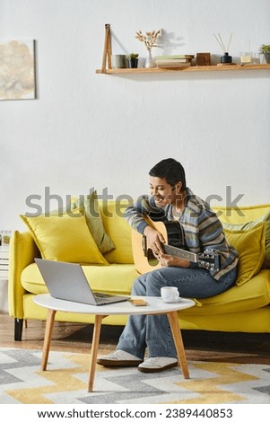 vertical shot of joyful young woman sitting on sofa with guitar looking on laptop on remote class. tattoo translation: sugar-free or no sugar