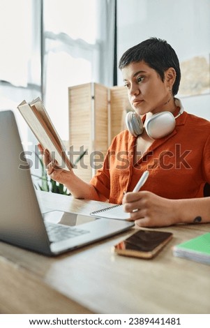 vertical shot of attractive woman in orange shirt taking notes and looking at book, education. tattoo translation: sugar-free or no sugar