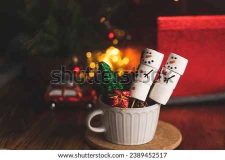 Marshlellow snowmen in a mug. Hot chocolate with marshmallows. Christmas mood. Funny and cute snowmen in a coffee mug. Warm and cozy autumn. Close-up of the Christmas composition.