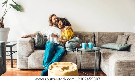 Cheerful multiracial couple sitting on sofa in the living room - Happy family moving in new home - Real estate and stylish furniture concept Royalty-Free Stock Photo #2389455387