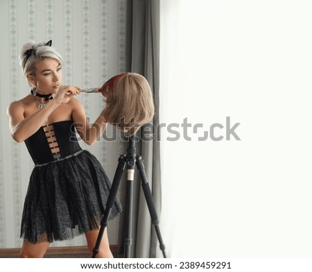 fashionable girl in stylish clothes paints her wig hair pink with a brush on the wig