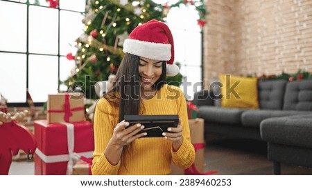 Young beautiful hispanic woman celebrating christmas looking photography at home