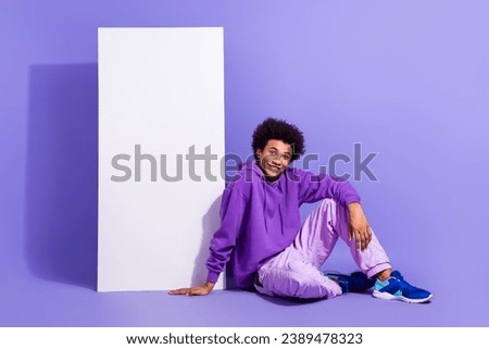 Full size photo of cheerful person wear violet hoodie sitting near smartphone screen empty space isolated on purple color background