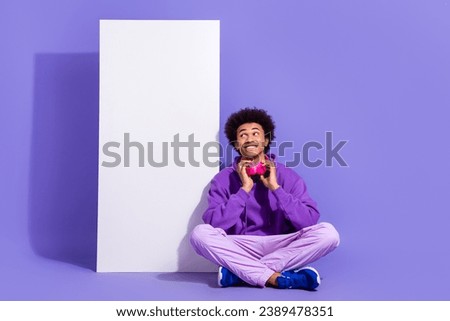 Full size photo of cheerful guy dressed stylish pullover look at smartphone screen touching earphones isolated on purple color background