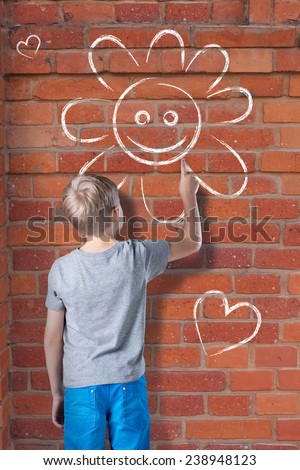 Little blond boy drawing by chalk on brick wall