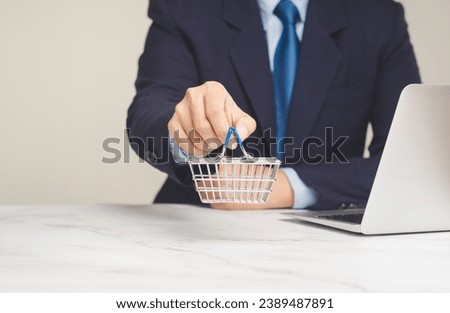 A small shopping basket in hand while sitting at the table in the office. Business and e-commerce concept. Close-up photo.