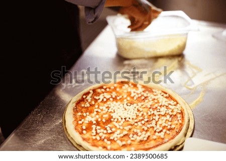 Faceless view of raw pizza with cheese near blurred chef in kitchen	
