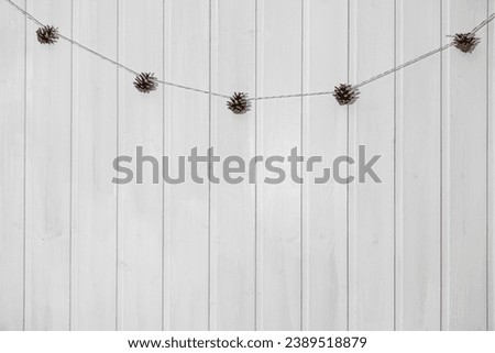 Simple Elegant DIY Christmas Decorations in Scandinavian Style. Minimal Christmas Natural Garland. Aesthetic Xmas Craft. Trendy Farmhouse Decor Idea. Cones Hanging against a White Wooden Wall
