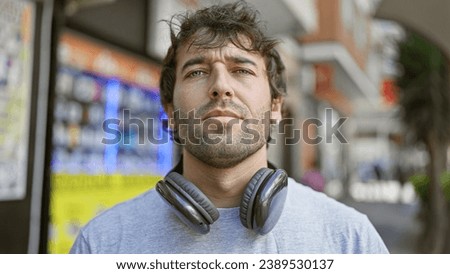 Cool young man rocking a beard, standing in sunlit city street, sportin' serious expression while wearing headphones, totally lost in his music Royalty-Free Stock Photo #2389530137