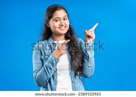 Portrait of a lovely attractive Indian girl gesturing with forefinger to the side over blue background