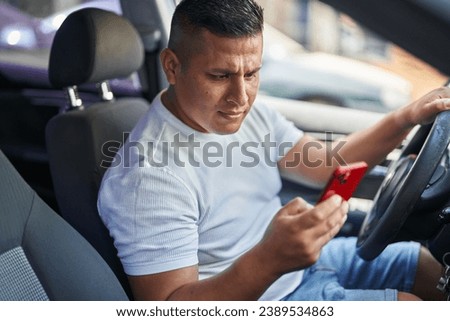 Young latin man using smartphone sitting on car at street