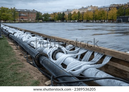 Preparation of outdoor skating rink for winter seasonal activity, pipeline pouring with water. Hoses of modern engineering systems for cooling close up. Skating rink and cooling systems installation