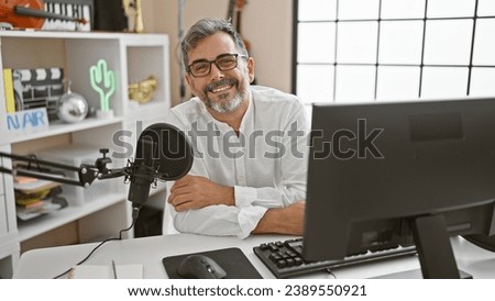 Young, attractive, grey-haired hispanic man smiling and masterfully presenting news on a live radio show inside a professional radio studio Royalty-Free Stock Photo #2389550921