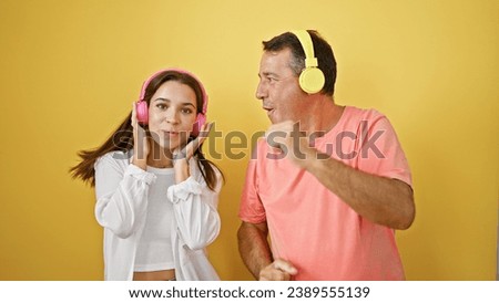 Father and daughter listening to music and dancing over isolated yellow background