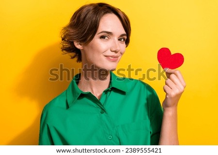 Photo of sweet adorable girl dressed green shirt showing little red heart isolated yellow color background