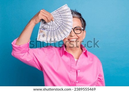Photo of positive funky woman with short hairdo dressed pink blouse money cover eye toothy smiling isolated on blue color background