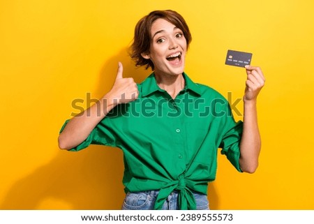 Photo of funky excited lady wear green shirt showing thumb up holding bank card isolated yellow color background